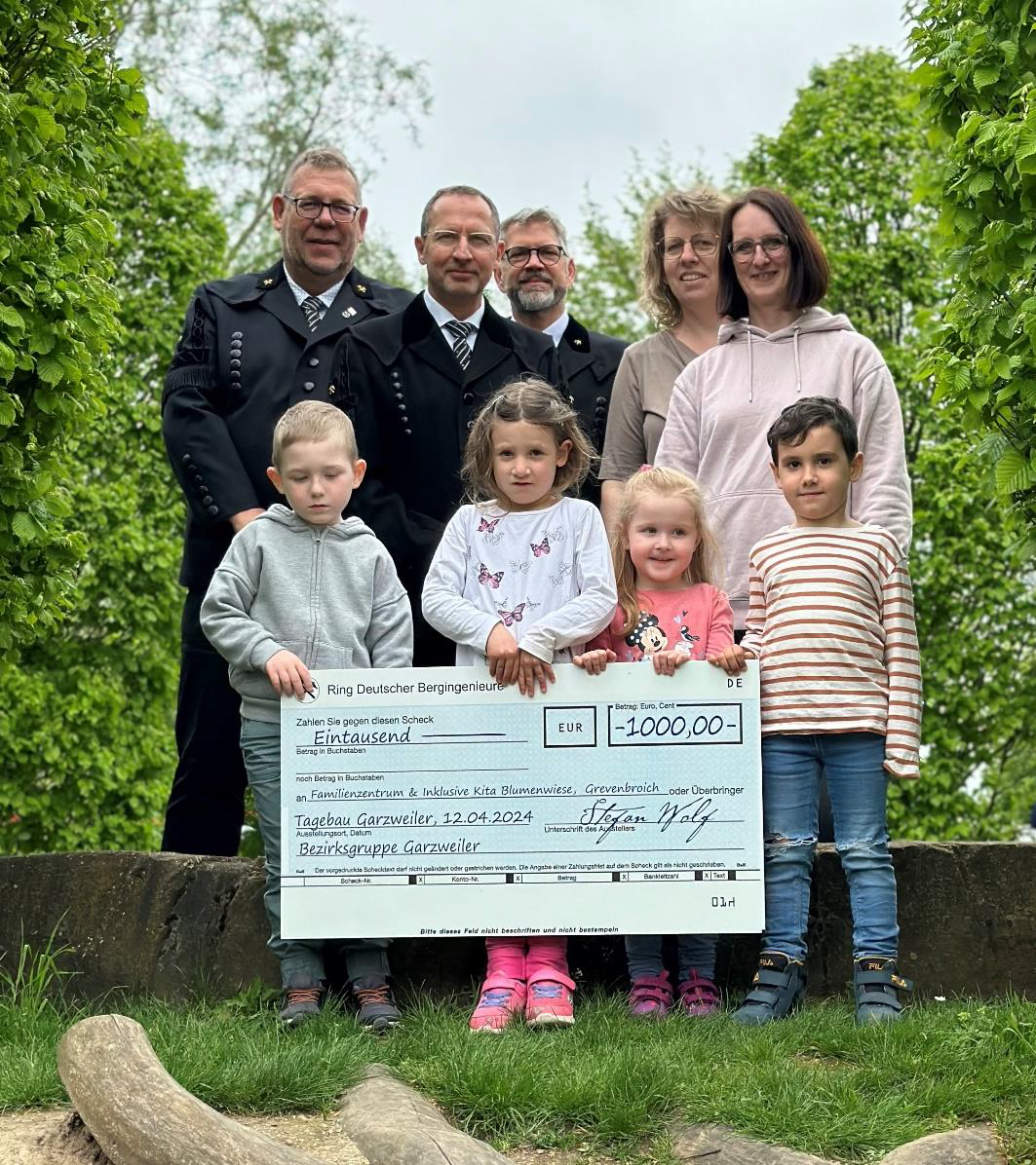 Vertreter der Bezirksgruppe Garzweiler mit Kindern und Erzieherinnen bei der Übergabe eines symbolischen Spendenschecks über 1.000 Euro an das Familienzentrum und die inklusive Kita Blumenwiese in Grevenbroich