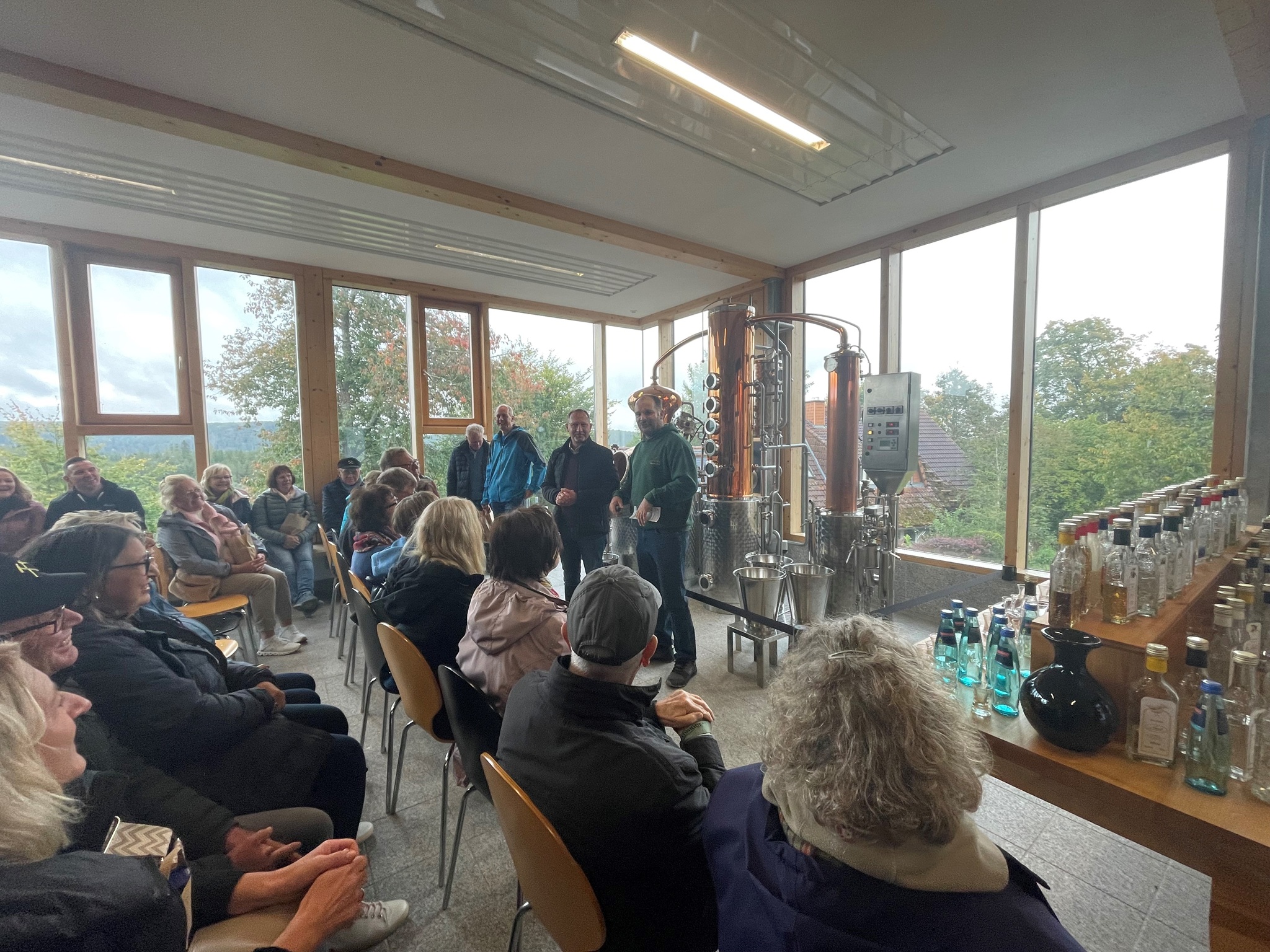 Besuchergruppe bei einer Führung durch eine Brennerei mit Verkostung: Vortrag vor einer Brennblase und einer Auswahl an Spirituosen