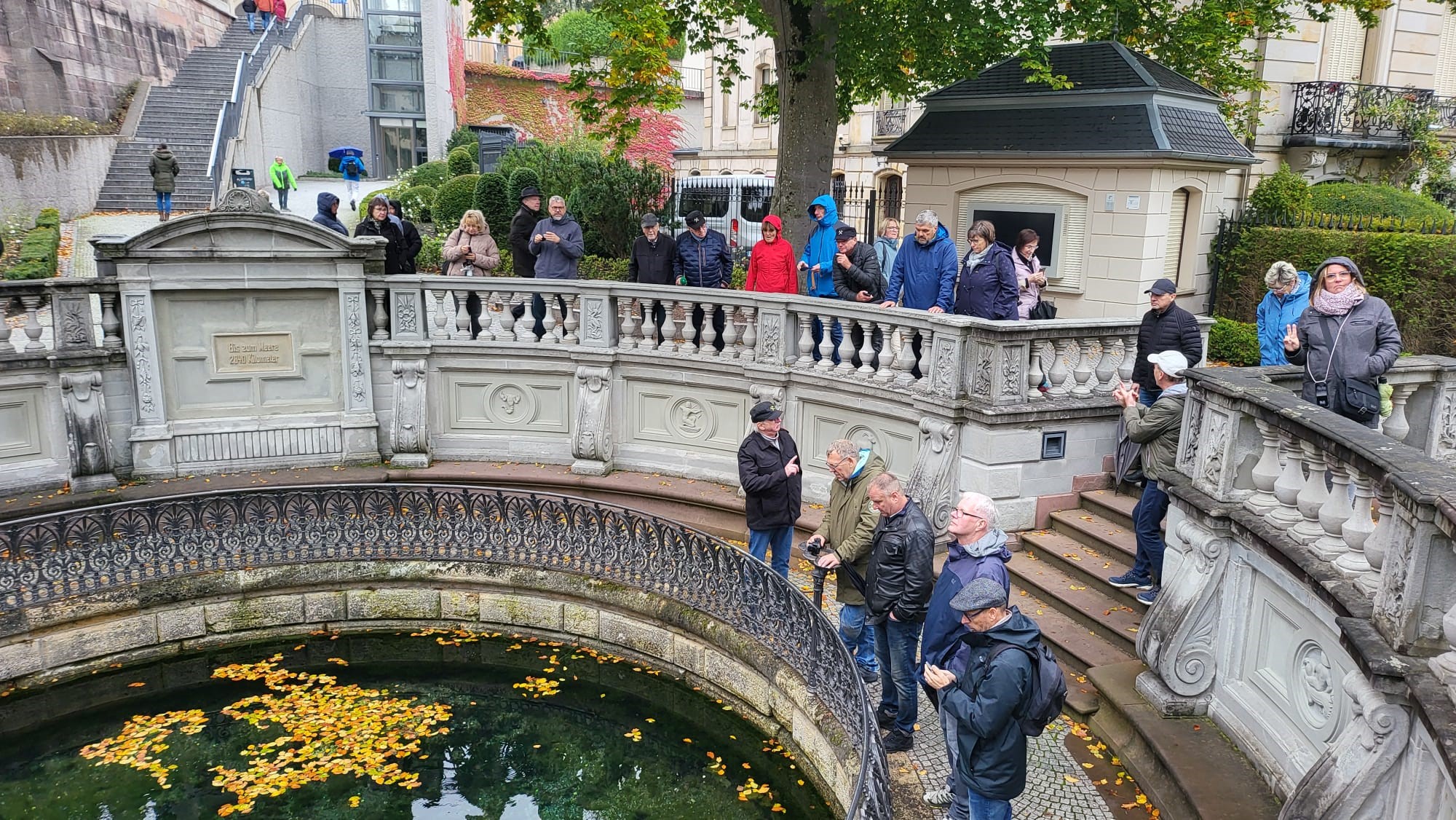 Gruppe von Besucherinnen und Besuchern an der Quelle des Jordanbachs in Bad Kissingen, umgeben von einer historischen Balustrade