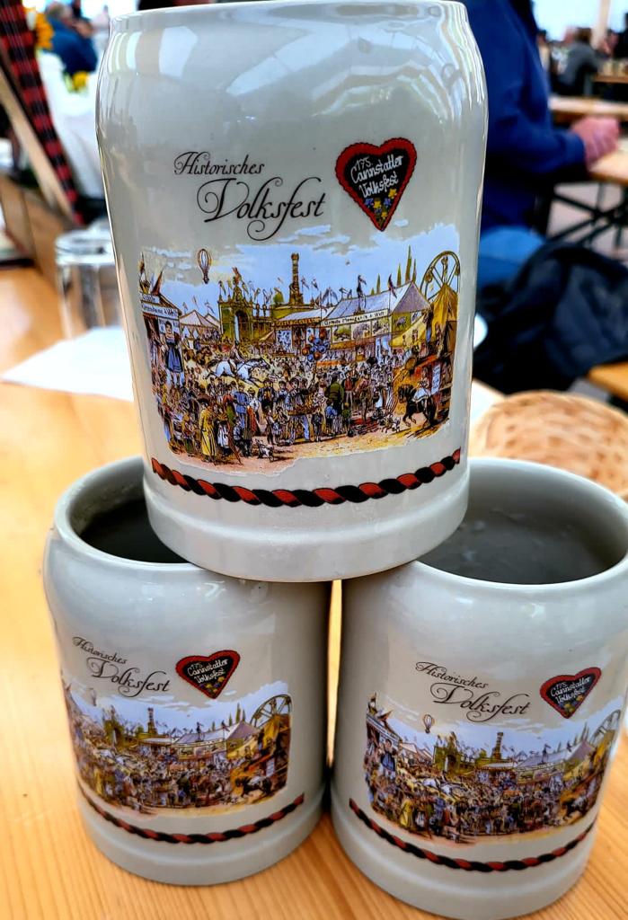 Drei Stein-Krüge mit Aufdruck „Historisches Volksfest“ und einer Illustration des Cannstatter Volksfestes auf einem Holztisch