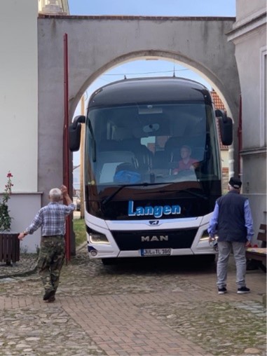 Ein Reisebus der Firma Langen fährt millimetergenau durch ein historisches Tor, zwei Männer helfen beim Einweisen