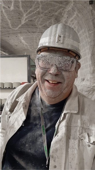 Bergmann mit Helm und Schutzbrille, komplett von weißem Staub bedeckt, lächelt in die Kamera